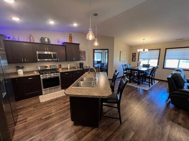 kitchen featuring a kitchen island with sink, a breakfast bar area, sink, stainless steel appliances, and hanging light fixtures