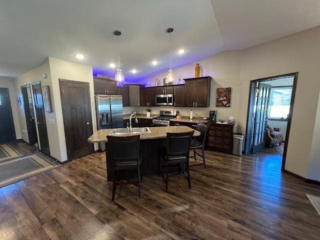 kitchen with hanging light fixtures, dark brown cabinets, a center island with sink, appliances with stainless steel finishes, and dark hardwood / wood-style flooring