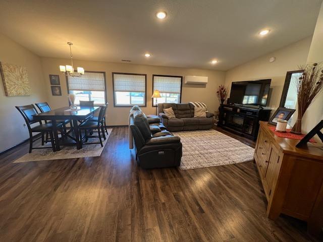 living room with dark wood-type flooring, a notable chandelier, a wall mounted air conditioner, and lofted ceiling