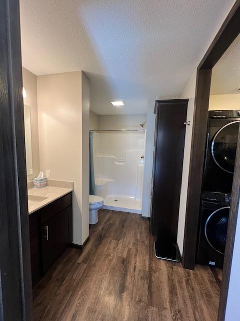 bathroom with vanity, walk in shower, hardwood / wood-style flooring, stacked washer / drying machine, and toilet