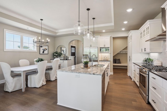 kitchen featuring a sink, a raised ceiling, wall chimney range hood, and appliances with stainless steel finishes