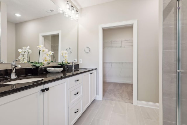 bathroom featuring baseboards, visible vents, a sink, double vanity, and a spacious closet