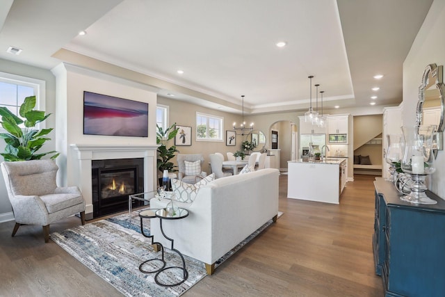 living room featuring recessed lighting, a glass covered fireplace, visible vents, wood finished floors, and a raised ceiling