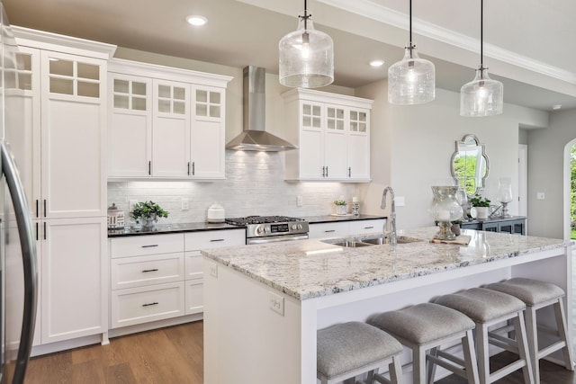 kitchen featuring wall chimney exhaust hood, decorative light fixtures, sink, stainless steel appliances, and white cabinets