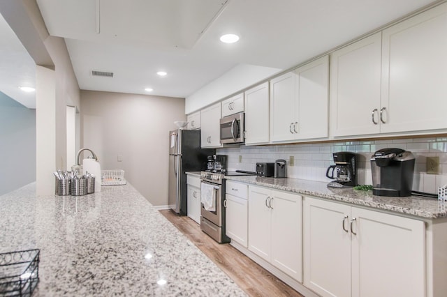 kitchen with light wood-type flooring, light stone counters, tasteful backsplash, white cabinetry, and appliances with stainless steel finishes