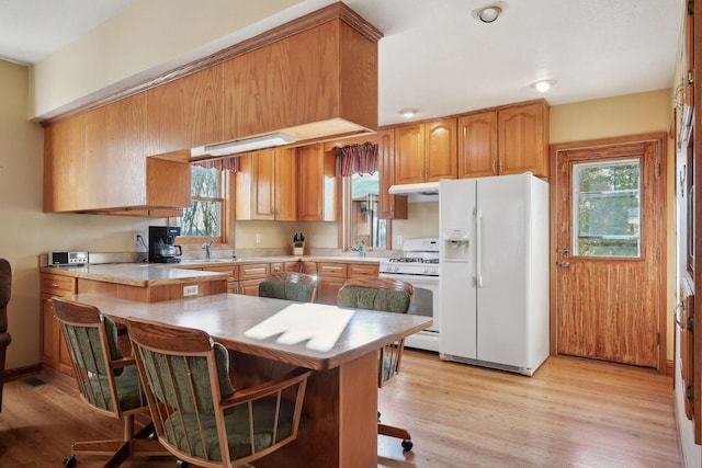 kitchen featuring white appliances, sink, light wood-type flooring, kitchen peninsula, and a kitchen breakfast bar