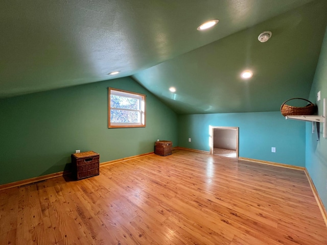 additional living space with lofted ceiling, light wood-type flooring, and a textured ceiling