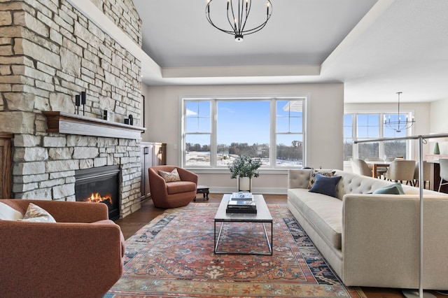 living room featuring a chandelier, a raised ceiling, a stone fireplace, and wood finished floors