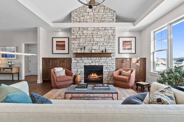 living room with vaulted ceiling, a stone fireplace, baseboards, and wood finished floors