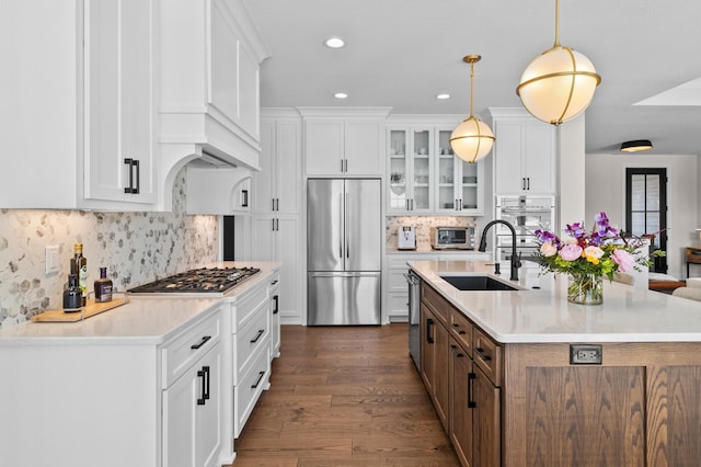 kitchen featuring a sink, stainless steel appliances, white cabinetry, a center island with sink, and glass insert cabinets