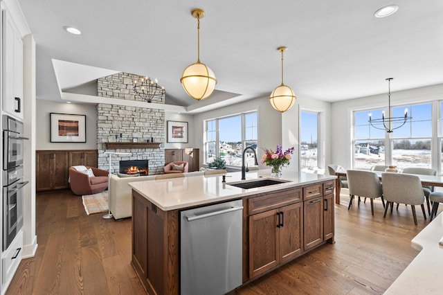 kitchen featuring a stone fireplace, dark wood-style floors, a chandelier, a sink, and stainless steel appliances