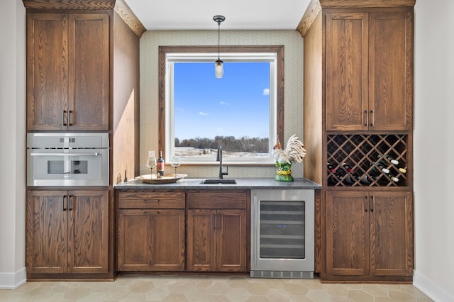 bar featuring pendant lighting, oven, beverage cooler, baseboards, and a sink
