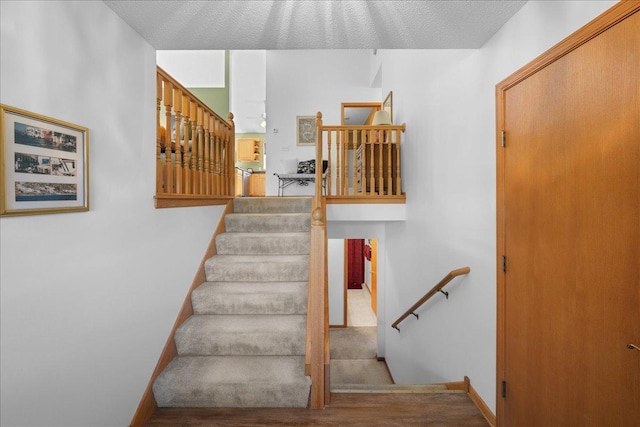 staircase with a textured ceiling and wood-type flooring