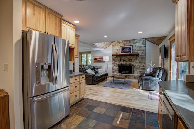 kitchen featuring light brown cabinetry, dark hardwood / wood-style flooring, a stone fireplace, lofted ceiling, and stainless steel refrigerator with ice dispenser