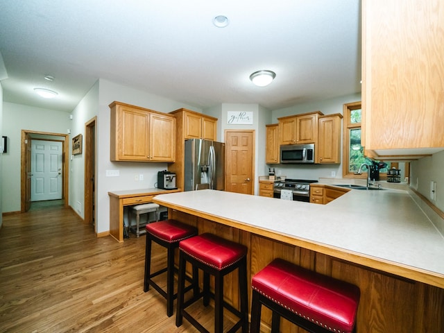 kitchen with kitchen peninsula, stainless steel appliances, sink, a breakfast bar, and dark hardwood / wood-style flooring