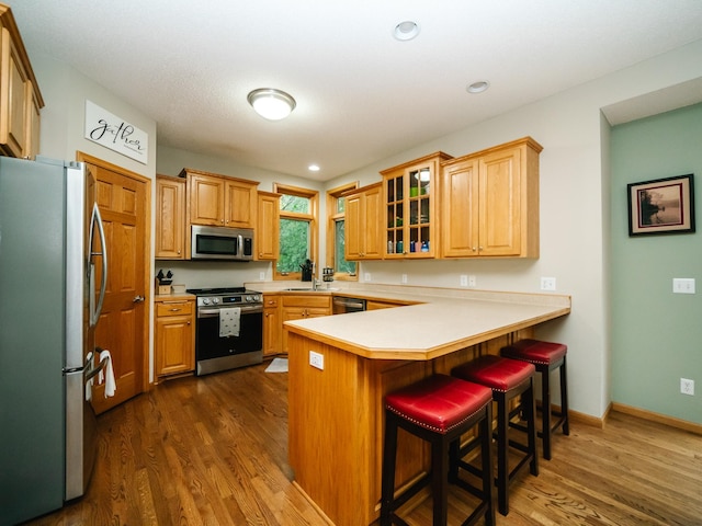 kitchen with sink, kitchen peninsula, stainless steel appliances, dark wood-type flooring, and a breakfast bar area