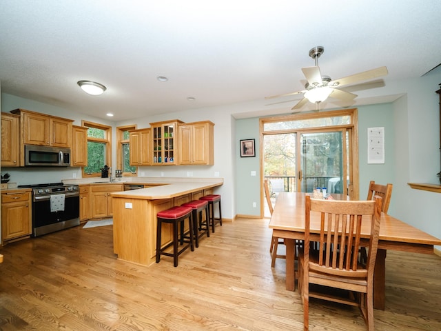 kitchen with kitchen peninsula, ceiling fan, a kitchen breakfast bar, light hardwood / wood-style floors, and stainless steel appliances