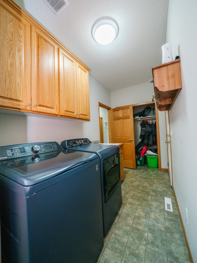 laundry room with a textured ceiling, cabinets, and washer and clothes dryer