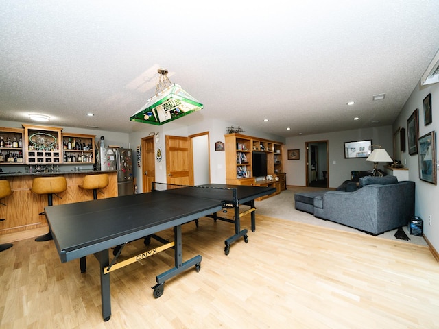 rec room with a textured ceiling, indoor bar, and light wood-type flooring