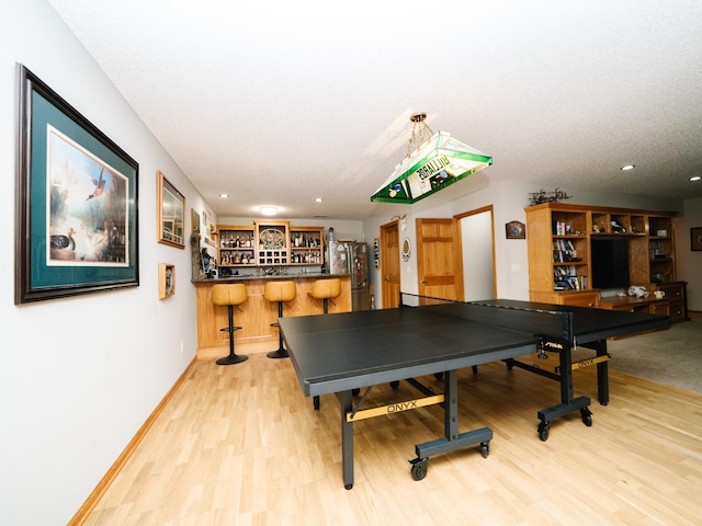 rec room with a textured ceiling, indoor bar, and hardwood / wood-style flooring