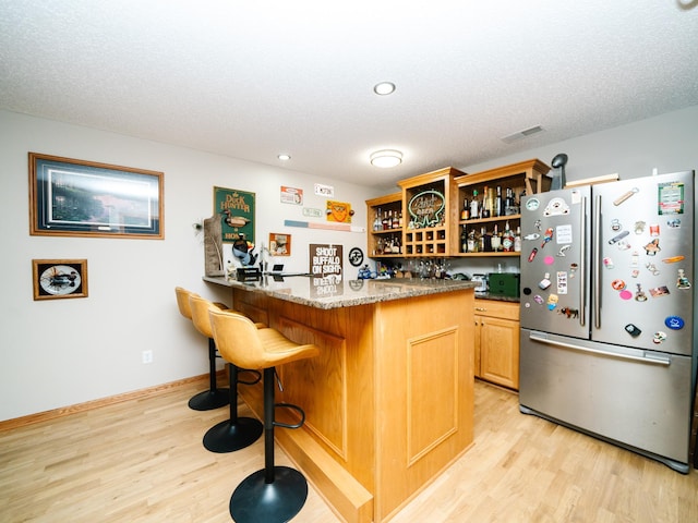 kitchen featuring a breakfast bar area, kitchen peninsula, light wood-type flooring, stone counters, and stainless steel refrigerator