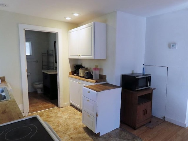 kitchen with butcher block countertops, light wood-type flooring, white cabinetry, and sink