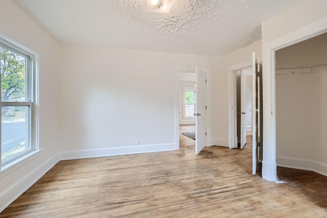 unfurnished bedroom featuring a textured ceiling, multiple windows, and light hardwood / wood-style flooring