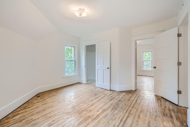 unfurnished bedroom with light hardwood / wood-style floors, vaulted ceiling, multiple windows, and a textured ceiling