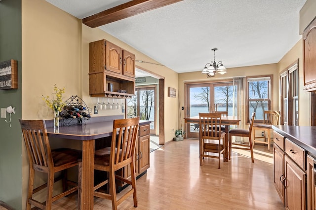 kitchen featuring a water view, a notable chandelier, a textured ceiling, light hardwood / wood-style flooring, and decorative light fixtures