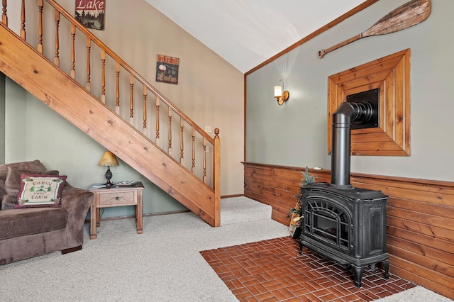 carpeted living room with high vaulted ceiling, wooden walls, and a wood stove