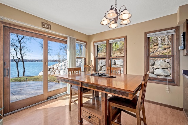 dining area featuring light hardwood / wood-style floors, a water view, an inviting chandelier, and a healthy amount of sunlight