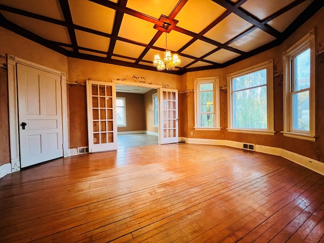 interior space with french doors, a notable chandelier, coffered ceiling, and light hardwood / wood-style flooring