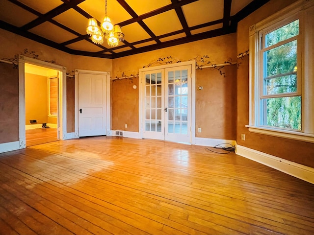 spare room with french doors, light hardwood / wood-style floors, coffered ceiling, and an inviting chandelier