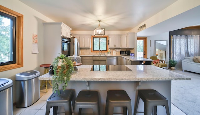 kitchen with light tile patterned floors, a breakfast bar area, a sink, black appliances, and a peninsula