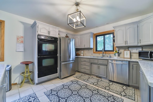kitchen with a sink, appliances with stainless steel finishes, a chandelier, gray cabinetry, and light tile patterned flooring