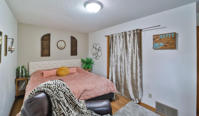 bedroom with visible vents, wood finished floors, and a textured ceiling