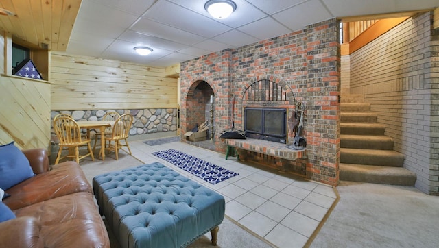 living area featuring brick wall, wooden walls, carpet flooring, and a drop ceiling