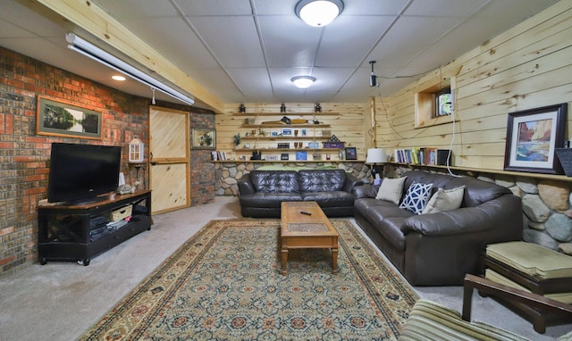 carpeted living area with wooden walls and a drop ceiling