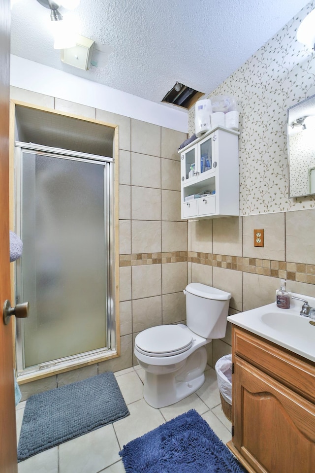 bathroom with tile patterned floors, a textured ceiling, a shower stall, and tile walls