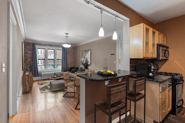 kitchen with kitchen peninsula, hanging light fixtures, black range with gas cooktop, hardwood / wood-style flooring, and a breakfast bar area