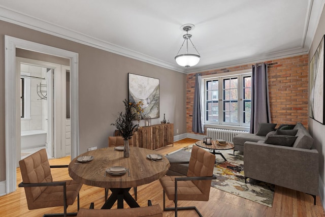 dining area featuring brick wall, crown molding, light hardwood / wood-style flooring, and radiator heating unit