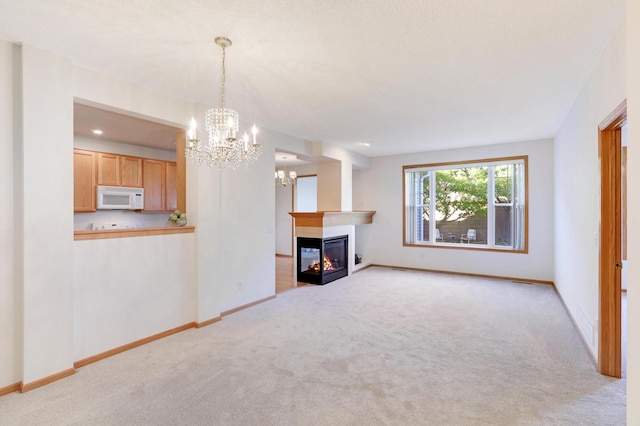 unfurnished living room with a multi sided fireplace, a notable chandelier, and light carpet