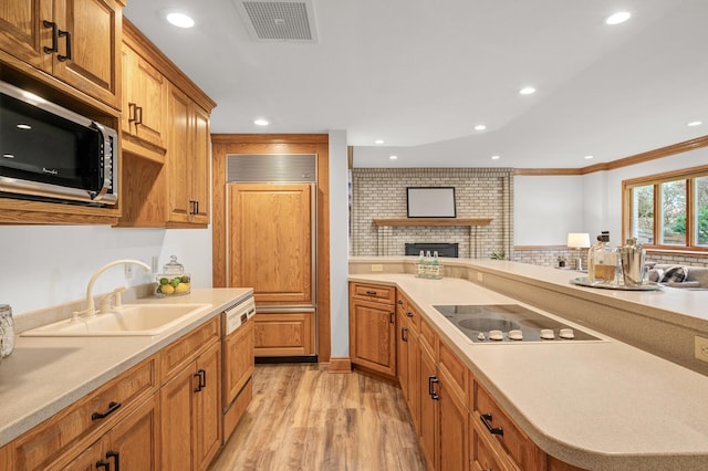 kitchen with ornamental molding, a fireplace, light hardwood / wood-style floors, sink, and paneled built in refrigerator