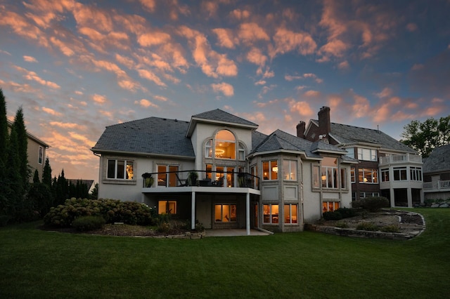 back house at dusk with a yard and a balcony