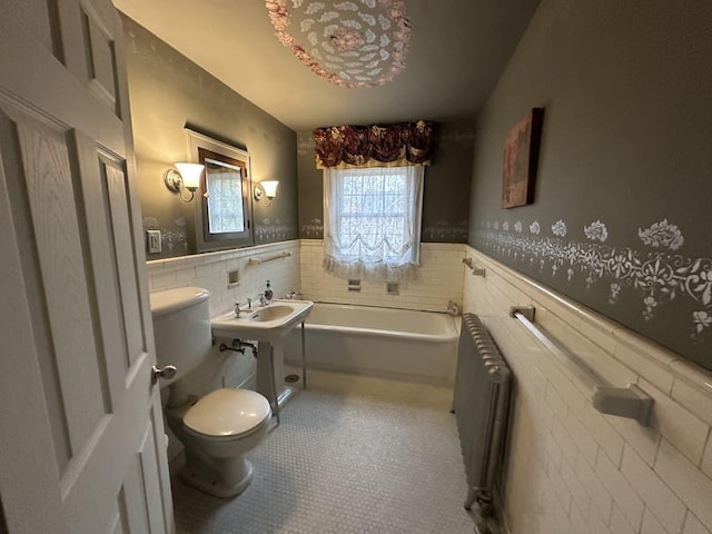 bathroom featuring radiator, a bathing tub, toilet, and tile walls