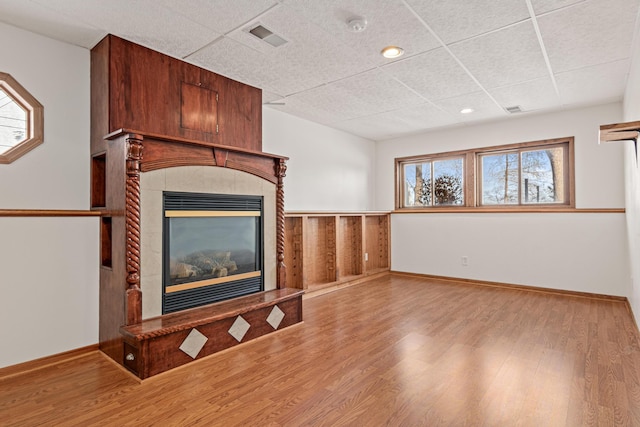 unfurnished living room featuring a tiled fireplace, wood-type flooring, and a drop ceiling