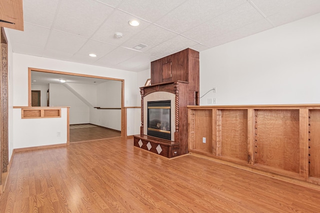 unfurnished living room featuring a fireplace, light hardwood / wood-style flooring, and a drop ceiling