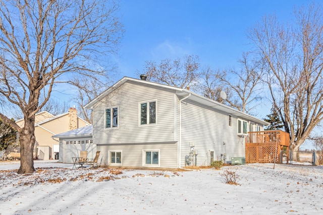 snow covered back of property with a garage and a deck