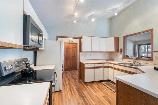 kitchen with vaulted ceiling, stainless steel appliances, light countertops, white cabinetry, and a sink