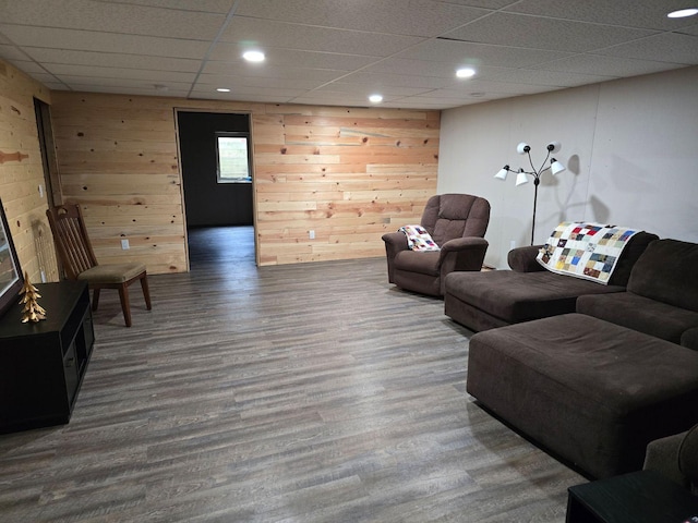 living room featuring a drop ceiling, hardwood / wood-style flooring, and wooden walls